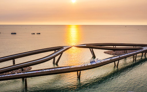 Kiss Bridge at sunset in Hon Thom, Phu Quoc, with people walking along the structure.