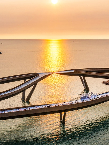 Kiss Bridge at sunset in Hon Thom, Phu Quoc, with people walking along the structure.