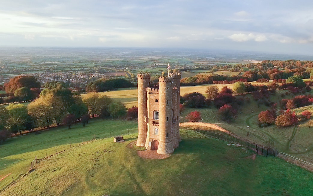 Broadway Tower in the Cotswolds countryside, England, surrounded by rolling hills.