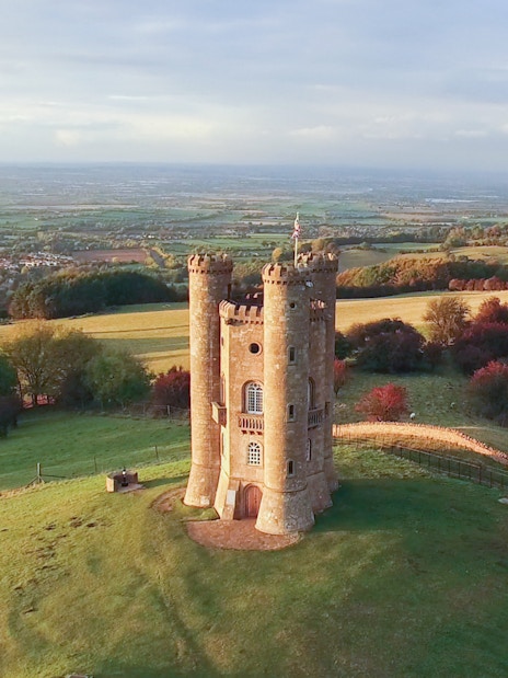 Broadway Tower in the Cotswolds countryside, England, surrounded by rolling hills.