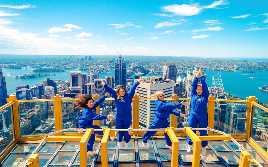 Group enjoying the view from Sydney Tower Eye Skywalk with cityscape and harbor in background.