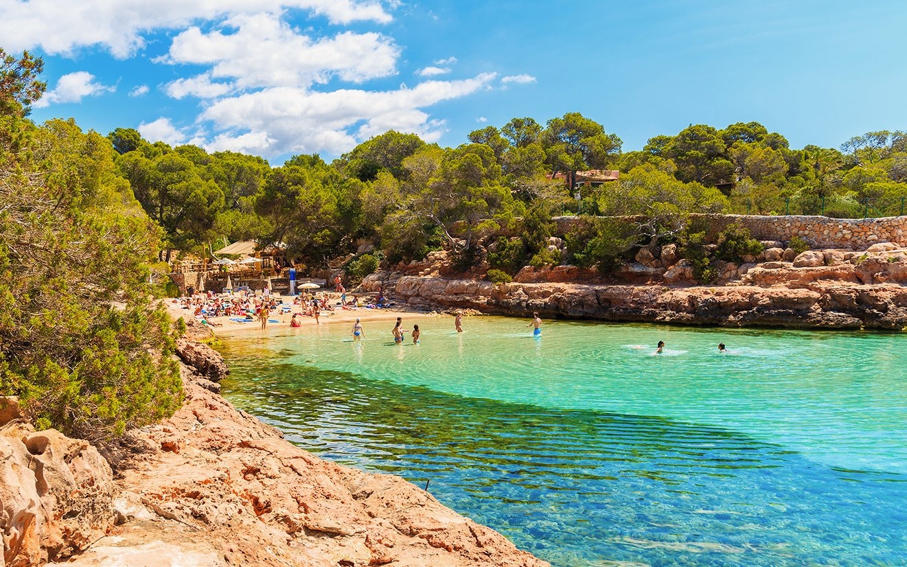 People swimming and sunbathing at Cala Gracioneta beach, Ibiza, Spain.