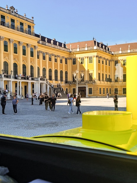 Panorama Train view of Schönbrunn Palace courtyard, Vienna, with visitors exploring.