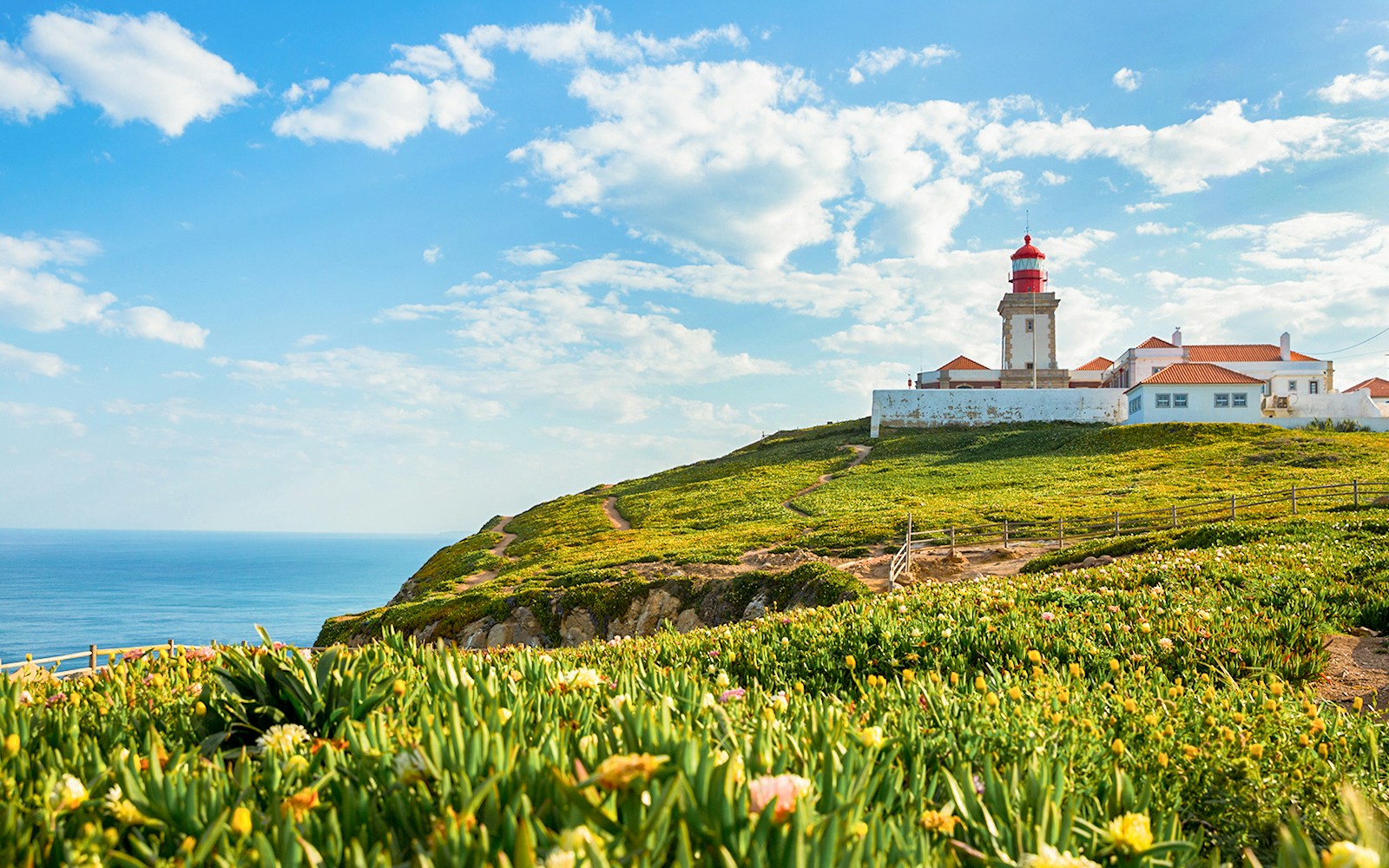 Cabo da Roca lighthouse on a cliff with ocean view and green landscape.