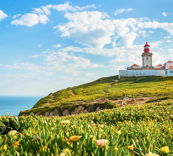 Cabo da Roca lighthouse on a cliff with ocean view and green landscape.