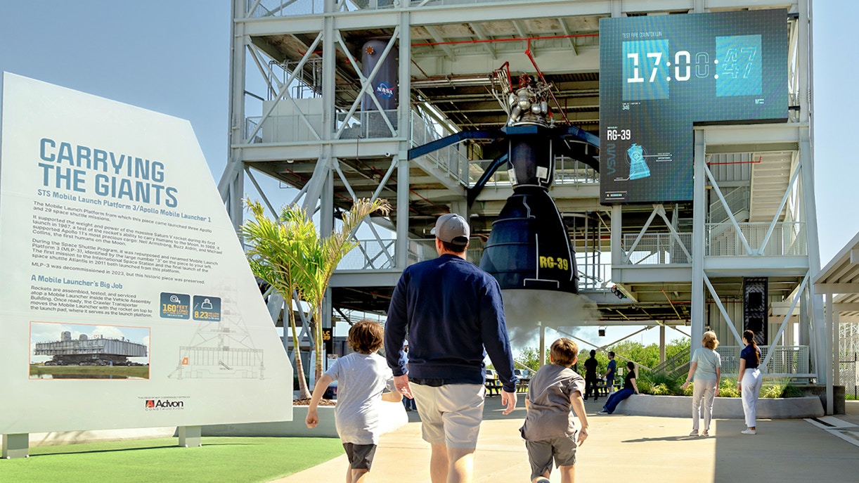 Family exploring Gantry at LC-39, Kennedy Space Center, with countdown display.