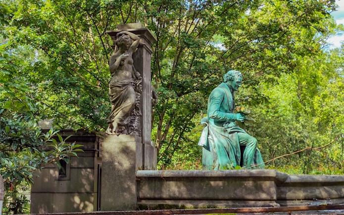 Statue of a seated figure and a standing sculpture at Père Lachaise Cemetery, Paris.