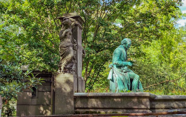 Statue of a seated figure and a standing sculpture at Père Lachaise Cemetery, Paris.