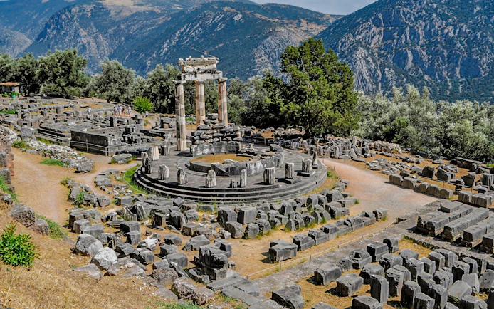 Ancient ruins of the Tholos of Delphi with mountainous backdrop in Greece.