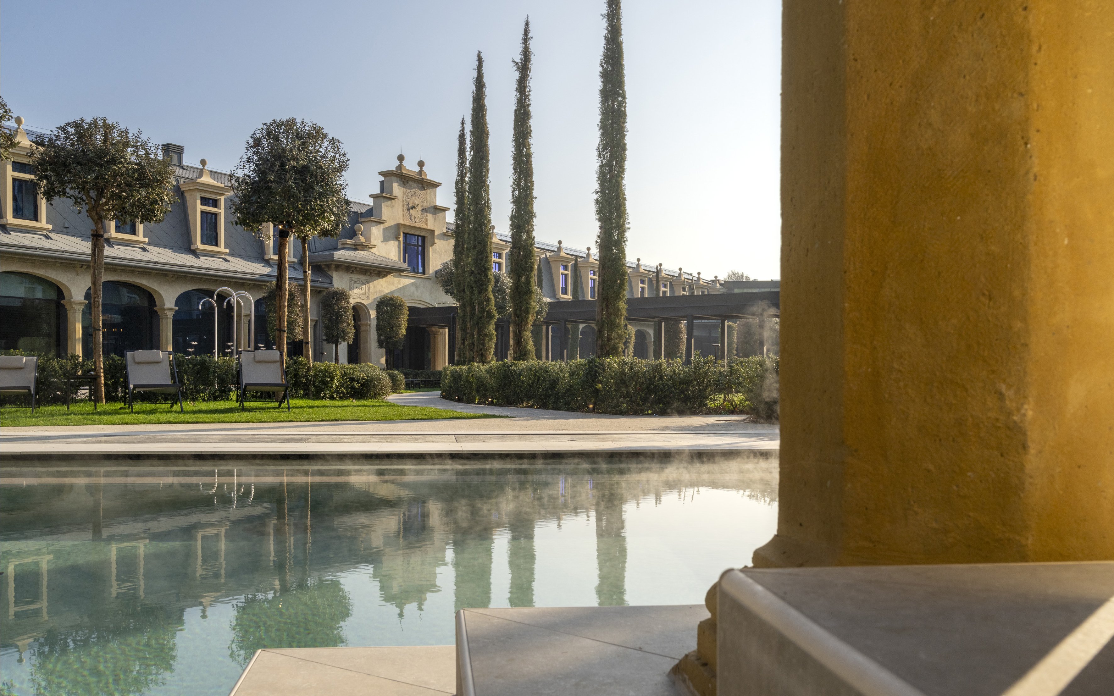 Outdoor pool area at Milan Wellness Spa with historic architecture and cypress trees.