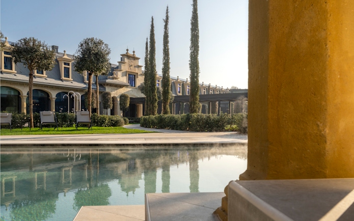 Outdoor pool area at Milan Wellness Spa with historic architecture and cypress trees.