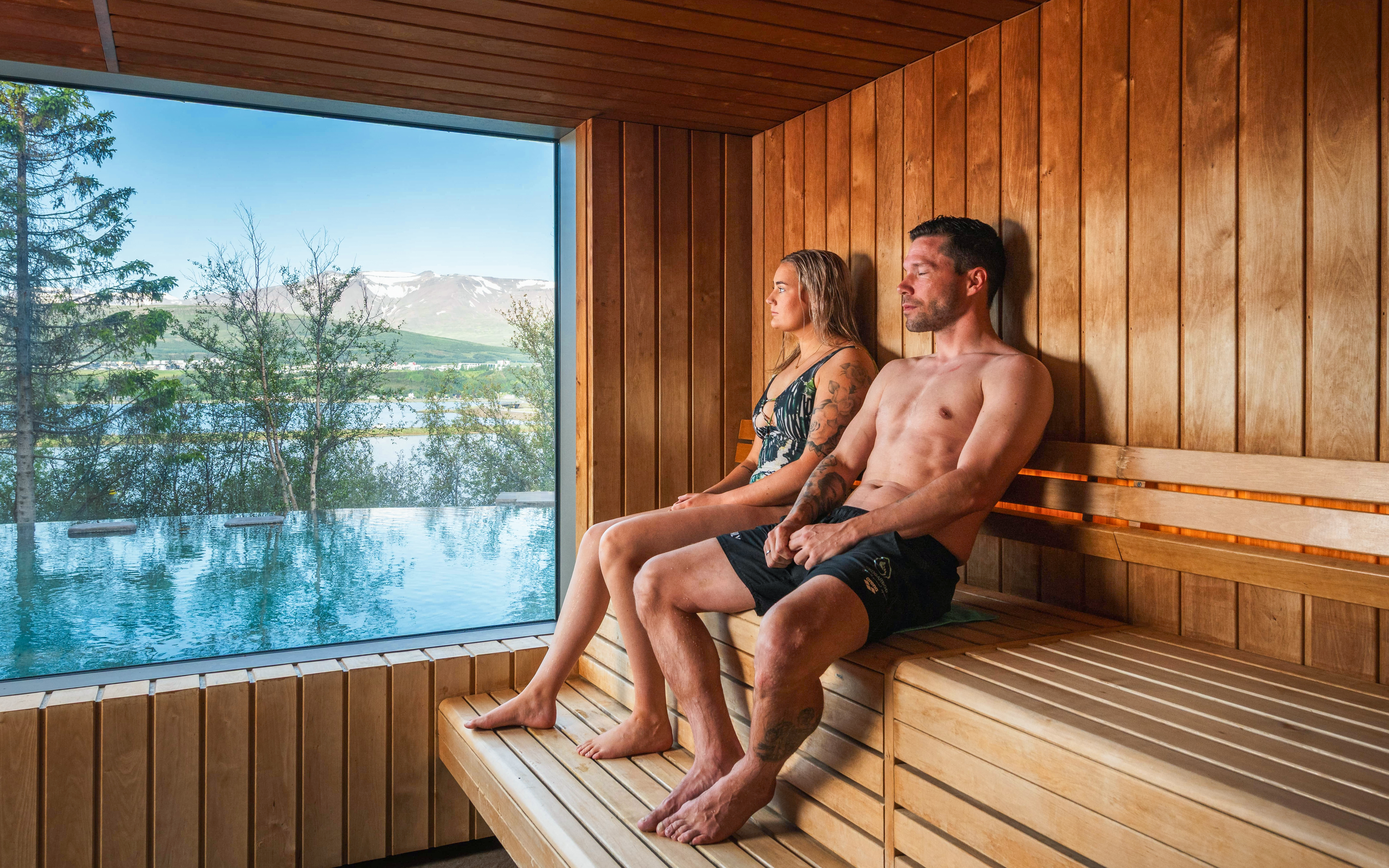 People relaxing in a sauna with a view of the Vaðlaskógur forest and geothermal spa in North Iceland.