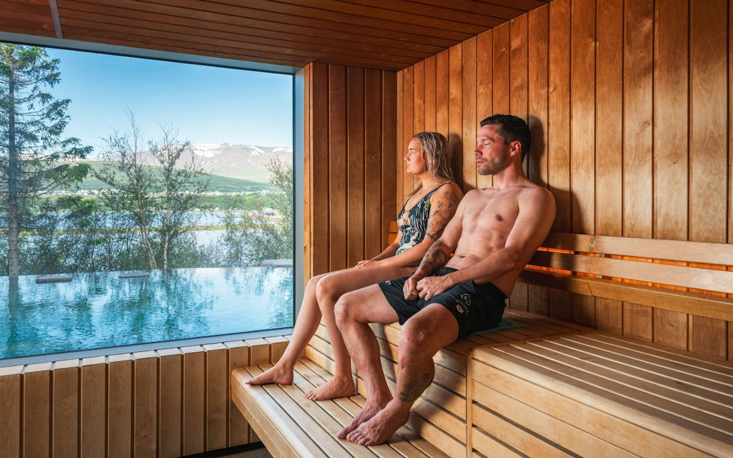 People relaxing in a sauna with a view of the Vaðlaskógur forest and geothermal spa in North Iceland.