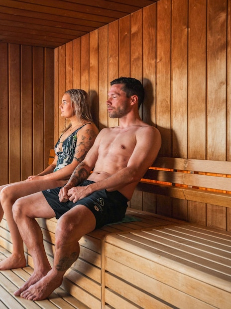 People relaxing in a sauna with a view of the Vaðlaskógur forest and geothermal spa in North Iceland.