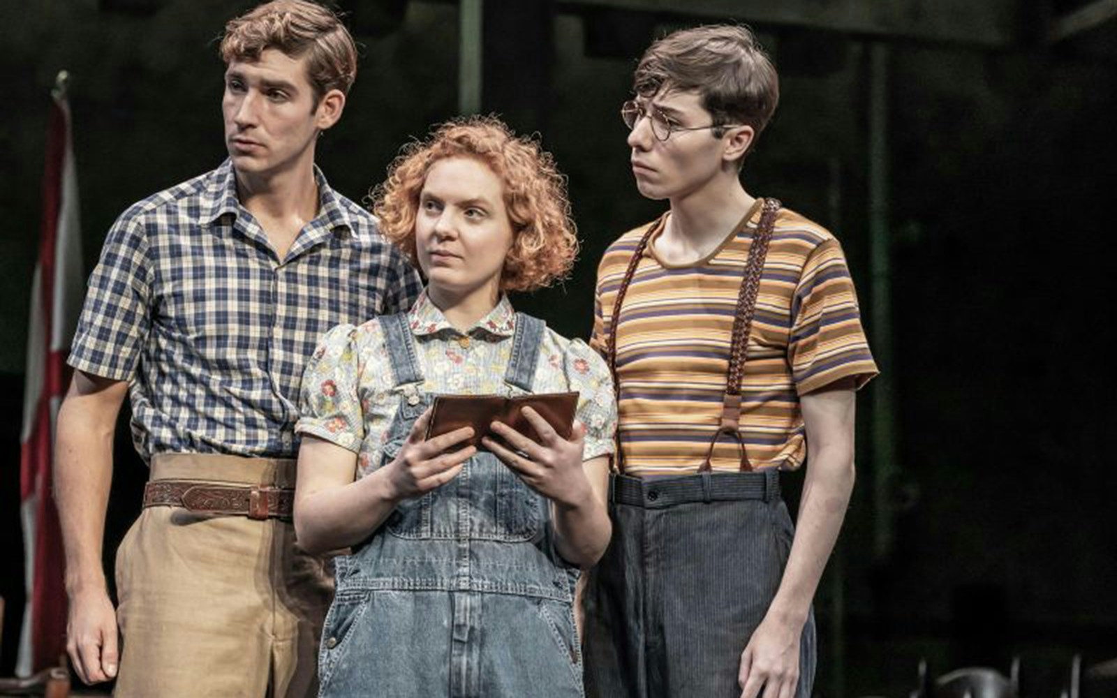 Three actors on stage in a scene from "To Kill A Mockingbird," one holding a book.