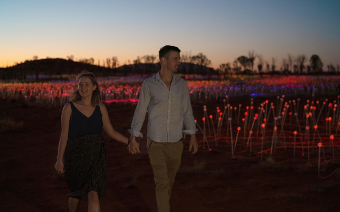 Couple walking through Field of Light installation at sunrise near Uluru.