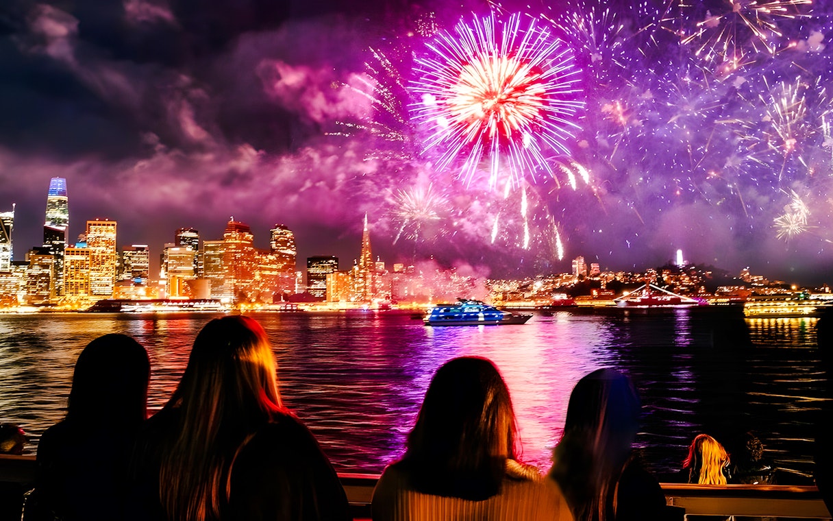 Guests watching fireworks over city skyline on New Year's Eve dinner cruise.