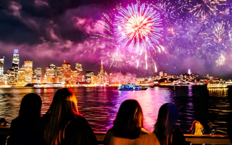 Guests watching fireworks over city skyline on New Year's Eve dinner cruise.