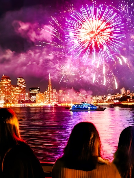 Guests watching fireworks over city skyline on New Year's Eve dinner cruise.