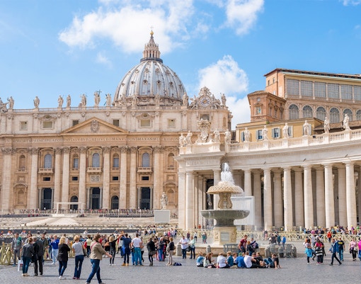 St. Peter's Square in Vatican City with tourists and the iconic St. Peter's Basilica in the background.