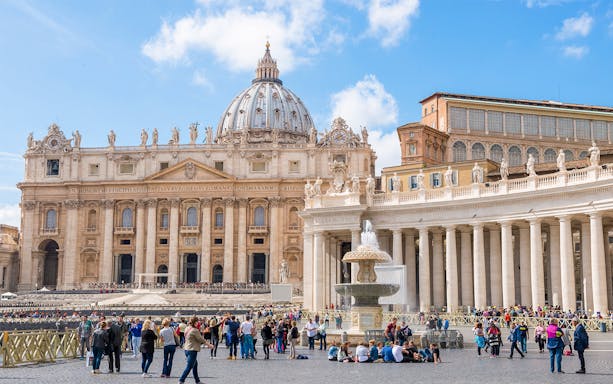 St. Peter's Square in Vatican City with tourists and the iconic St. Peter's Basilica in the background.