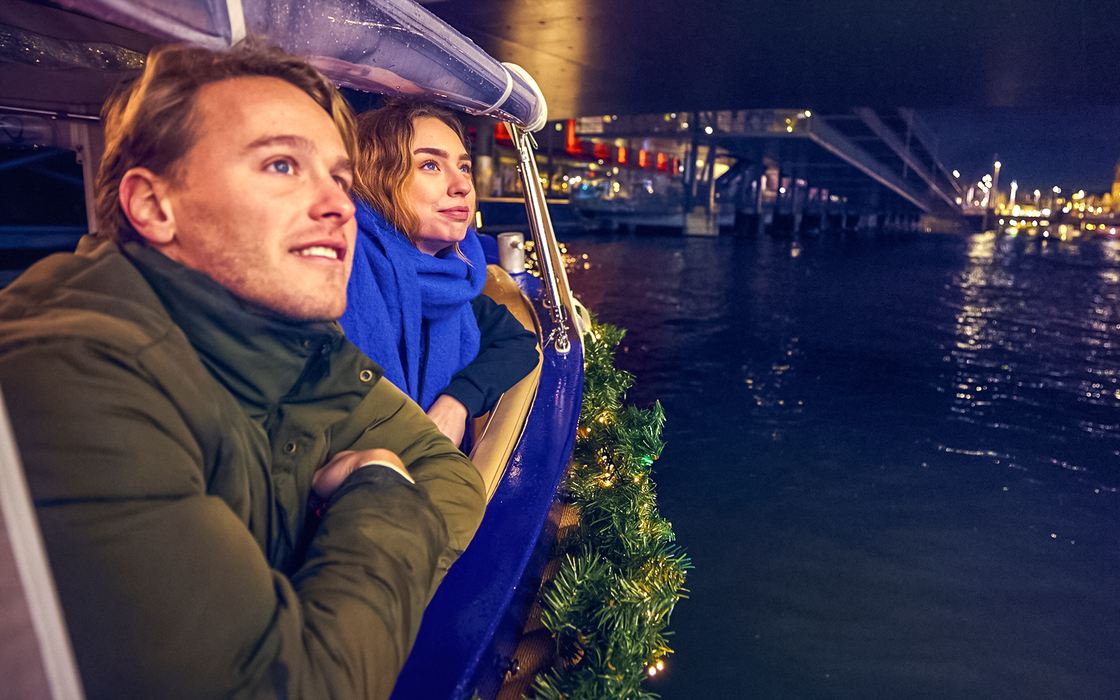 Couple enjoying Amsterdam Light Festival cruise with city lights reflecting on water.