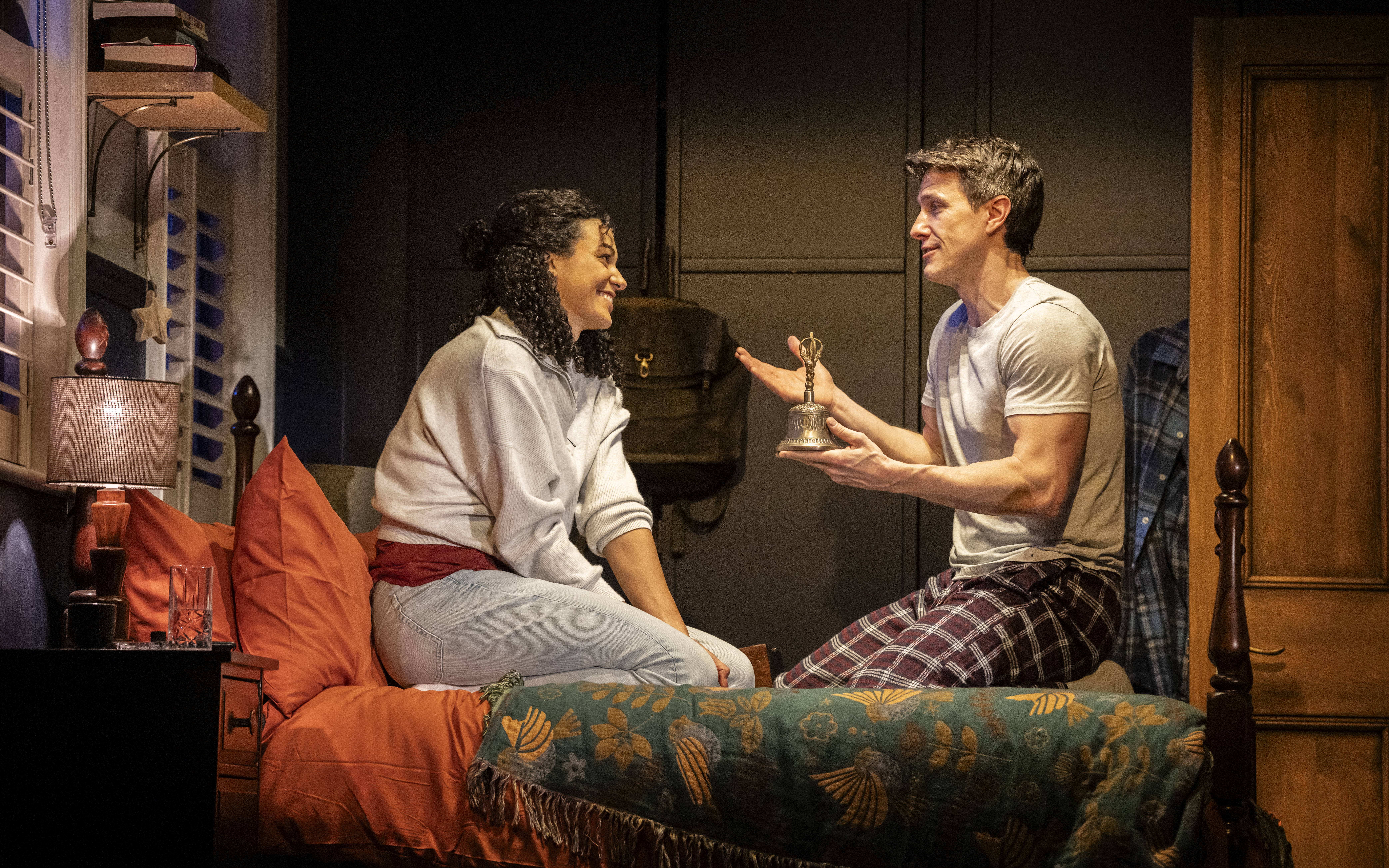 Stage scene from Paranormal Activity, Westend, with two actors on a bed discussing a bell.