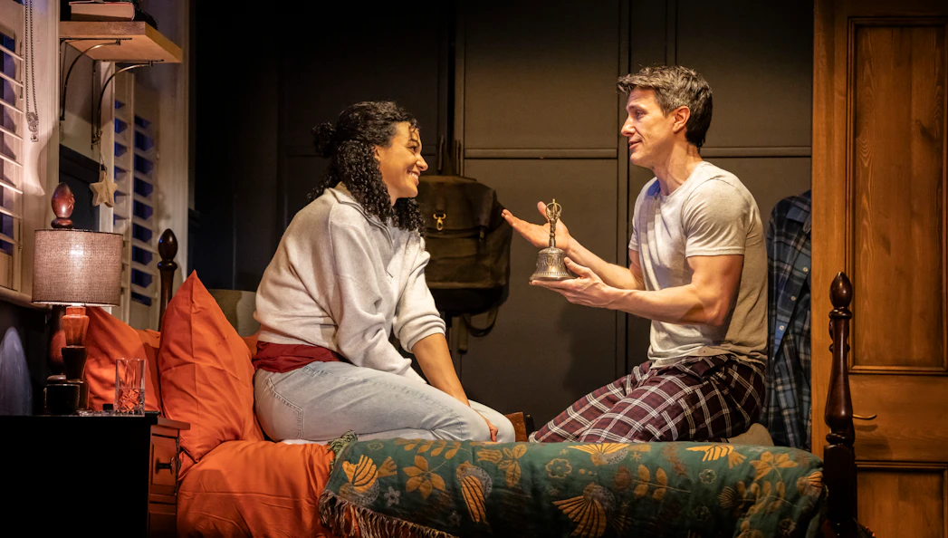 Stage scene from Paranormal Activity, Westend, with two actors on a bed discussing a bell.