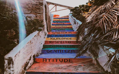 Colorful stairs with motivational words in Jericoacoara, Brazil, surrounded by tropical plants.