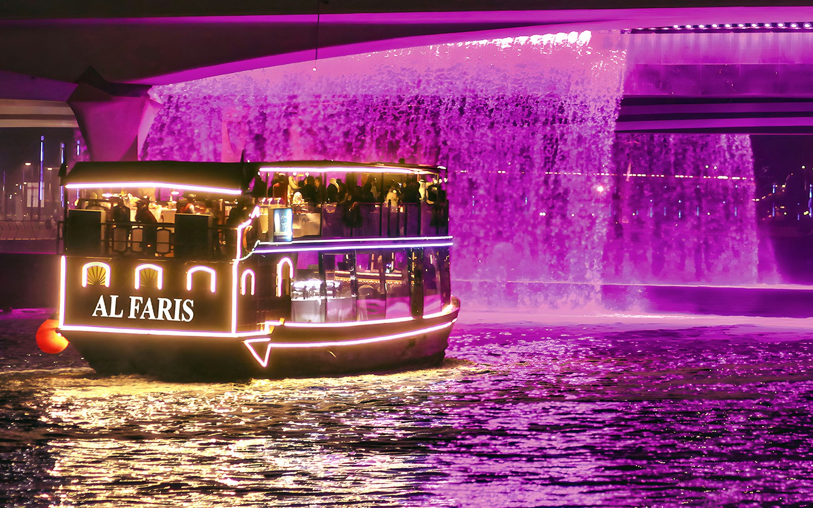 Dubai Water Canal cruise boat with illuminated lights under a purple waterfall.
