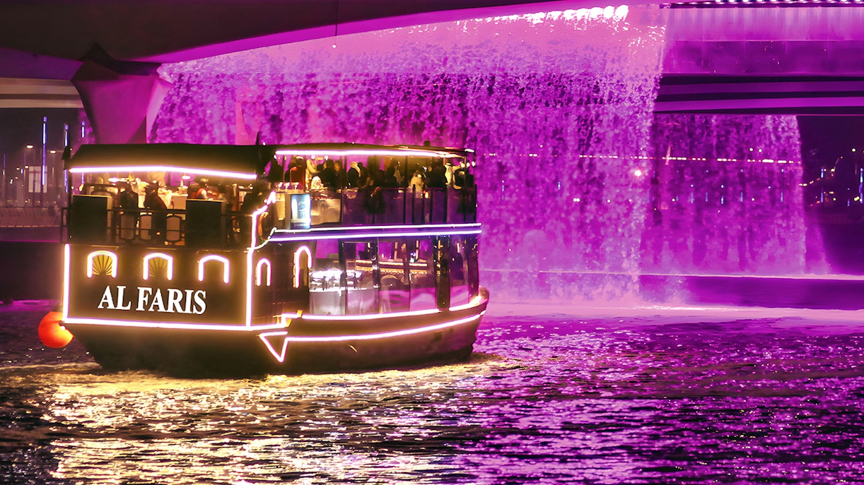 Dubai Water Canal cruise boat with illuminated lights under a purple waterfall.