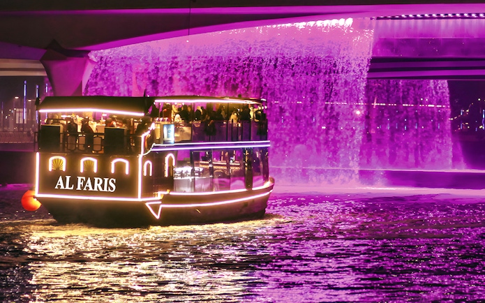 Dubai Water Canal cruise boat with illuminated lights under a purple waterfall.