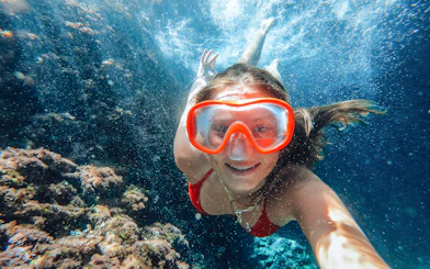 Snorkeler exploring underwater at Sunj Beach, vibrant coral in view.