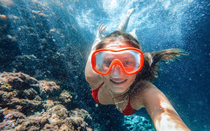 Snorkeler exploring underwater at Sunj Beach, vibrant coral in view.