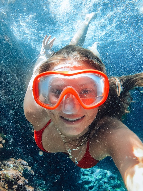 Snorkeler exploring underwater at Sunj Beach, vibrant coral in view.