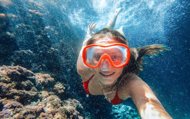 Snorkeler exploring underwater at Sunj Beach, vibrant coral in view.