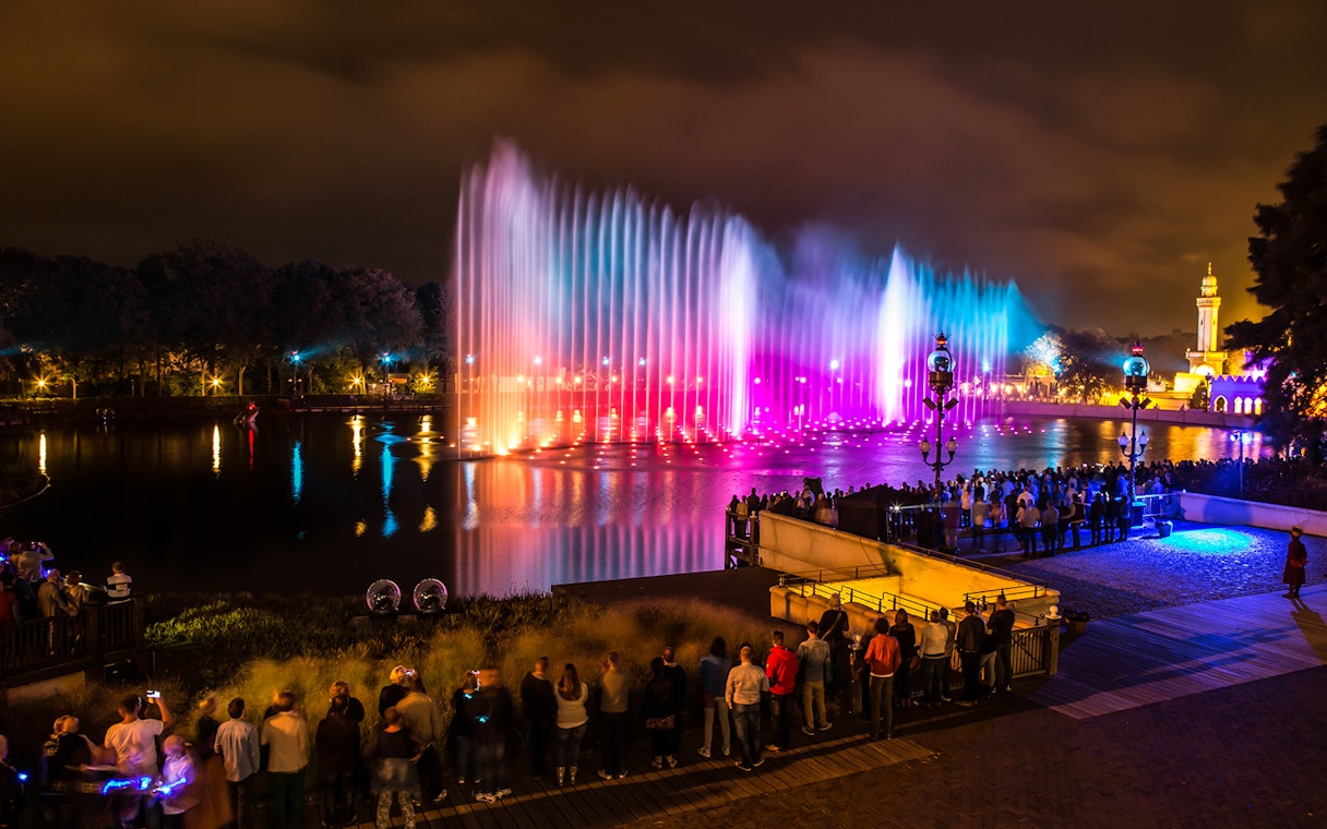 Crowd watching colorful fountain show at night in Efteling Theme Park, Netherlands.