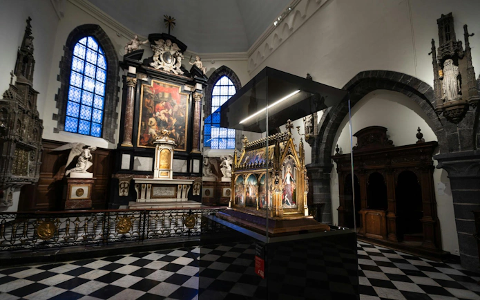 Interior of Museum Sint-Janshospitaal in Bruges with medieval altarpiece and stained glass windows.
