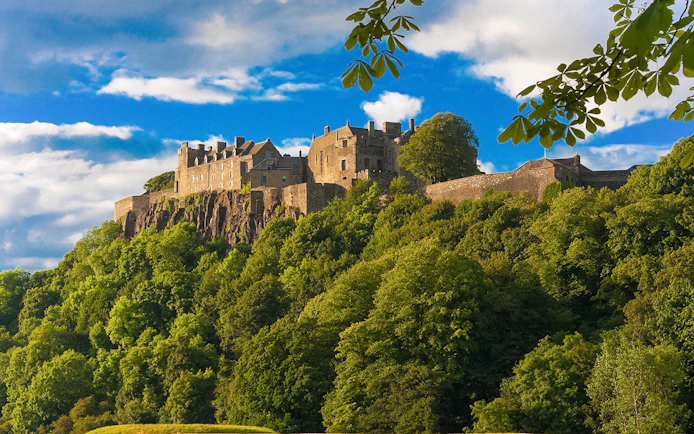 Stirling Castle surrounded by lush greenery under a blue sky in Scotland.