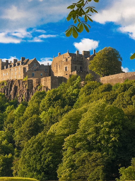 Stirling Castle surrounded by lush greenery under a blue sky in Scotland.