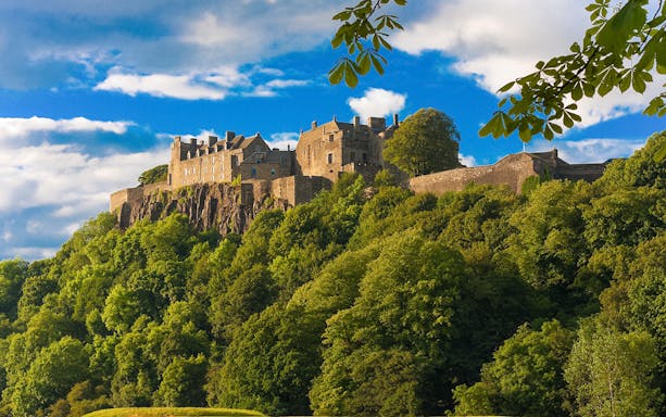 Stirling Castle surrounded by lush greenery under a blue sky in Scotland.