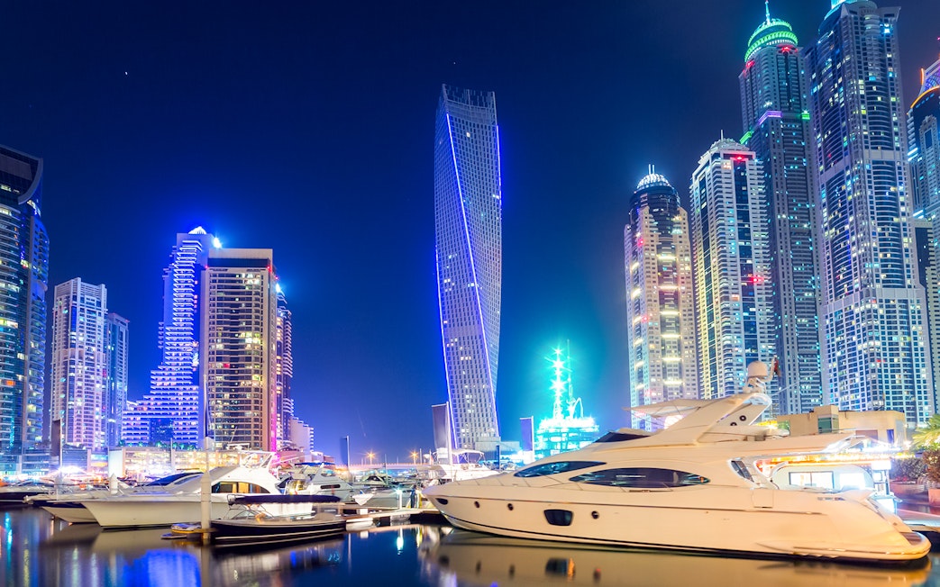 Cayan Tower illuminated at night with yachts in Dubai Marina.