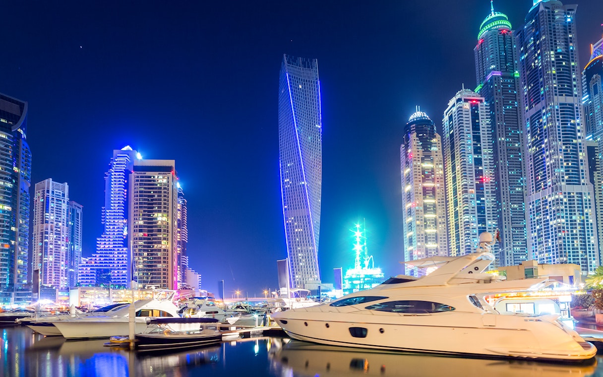 Cayan Tower illuminated at night with yachts in Dubai Marina.