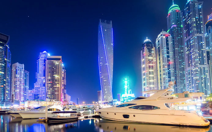 Cayan Tower illuminated at night with yachts in Dubai Marina.
