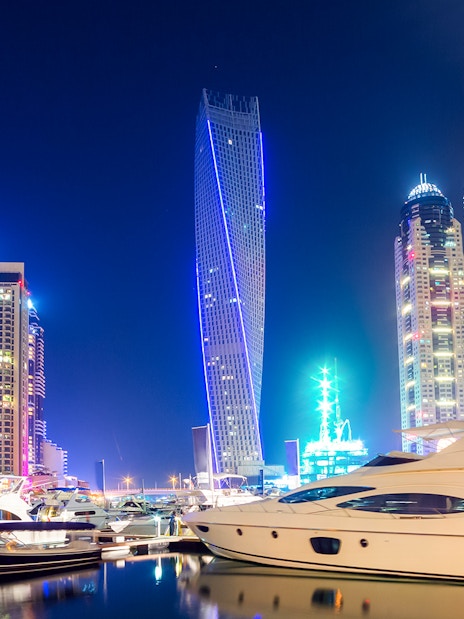 Cayan Tower illuminated at night with yachts in Dubai Marina.