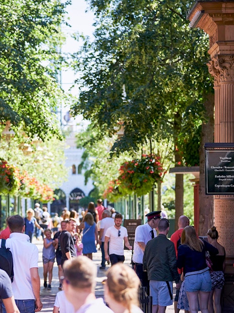 Visitors entering Tivoli Gardens in Copenhagen under ornate arches with lush greenery.