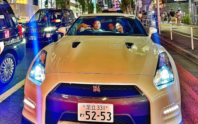 Tokyo street with Nissan GT-R R35, passengers enjoying JDM experience, surrounded by city lights.