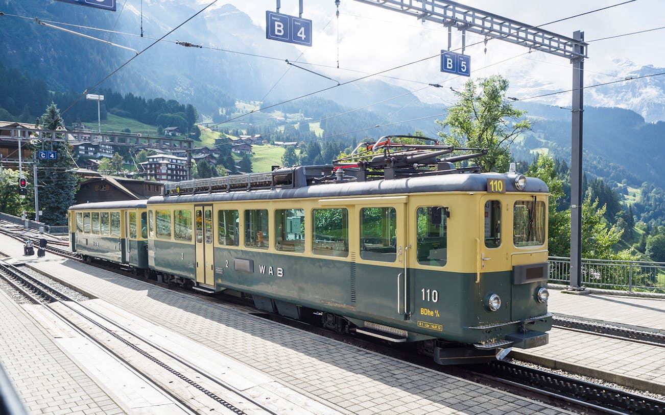 Swiss train at station with mountain backdrop on Basel-Jungfraujoch route.