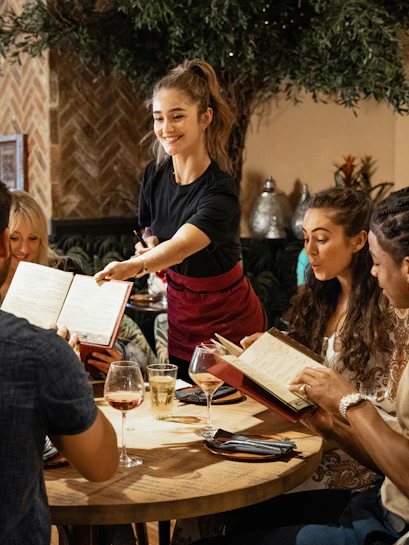 Group dining at a cozy restaurant with a server handing menus.