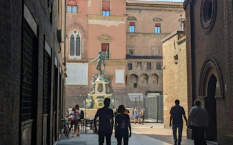 People walking towards the Fountain of Neptune in Bologna during a city exploration game.